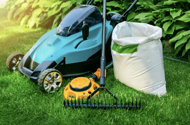 push lawnmower with rake, sprinkler and fertilizer bag in yard
